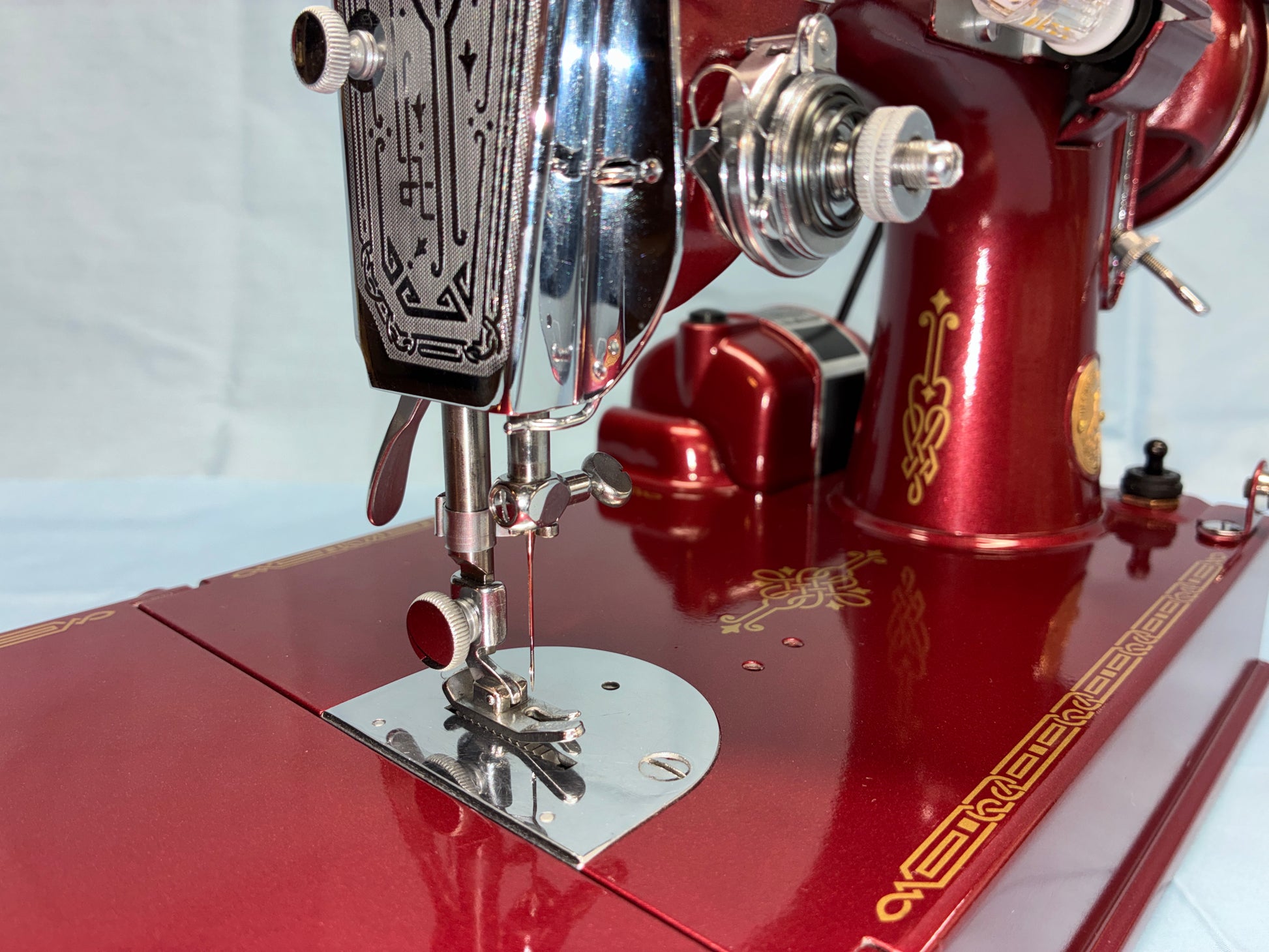 Close-up of a red sewing machine with metallic parts on a white background